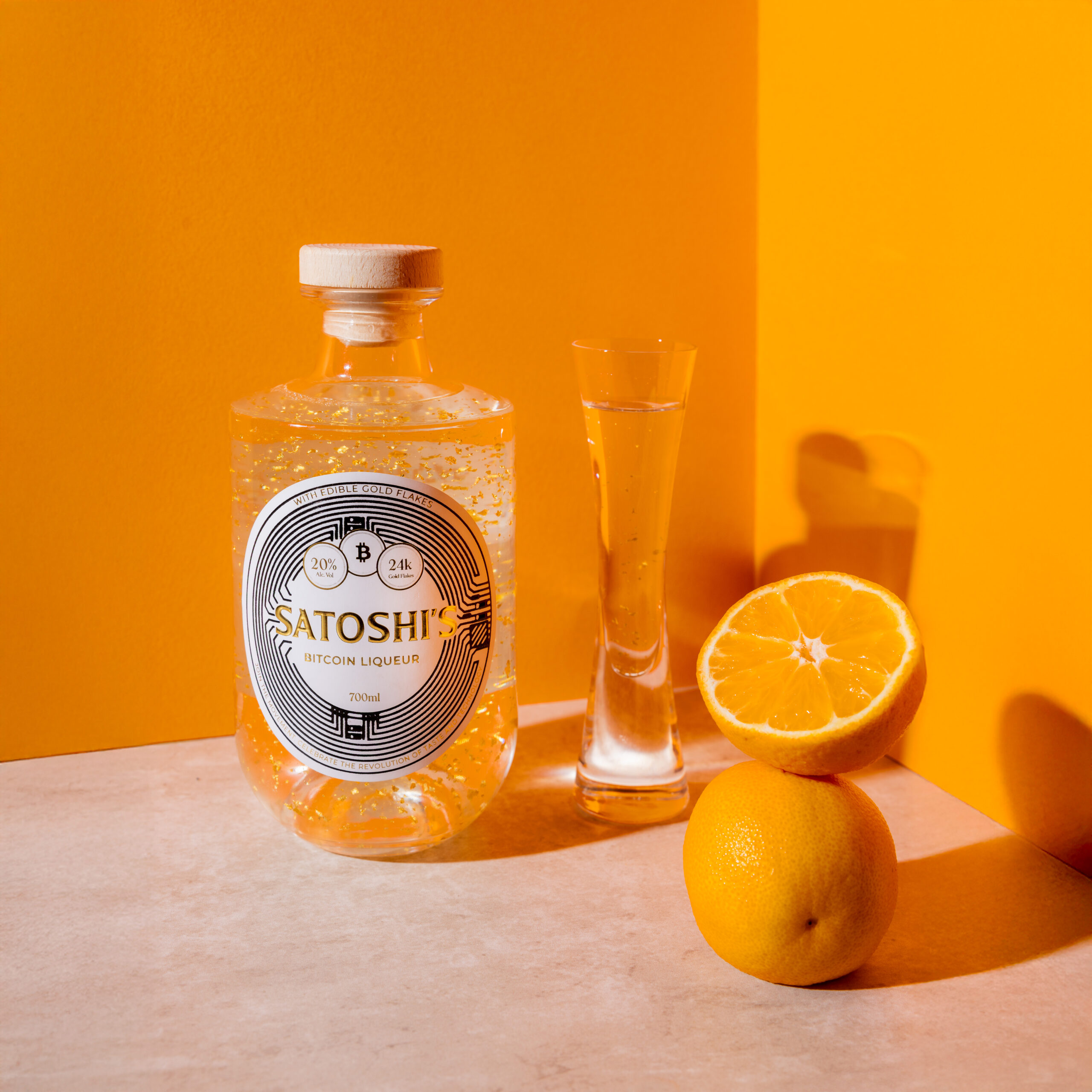 Satoshi’s Bitcoin Liqueur bottle displayed with sliced oranges on a bright yellow background, highlighting premium citrus-infused branding.