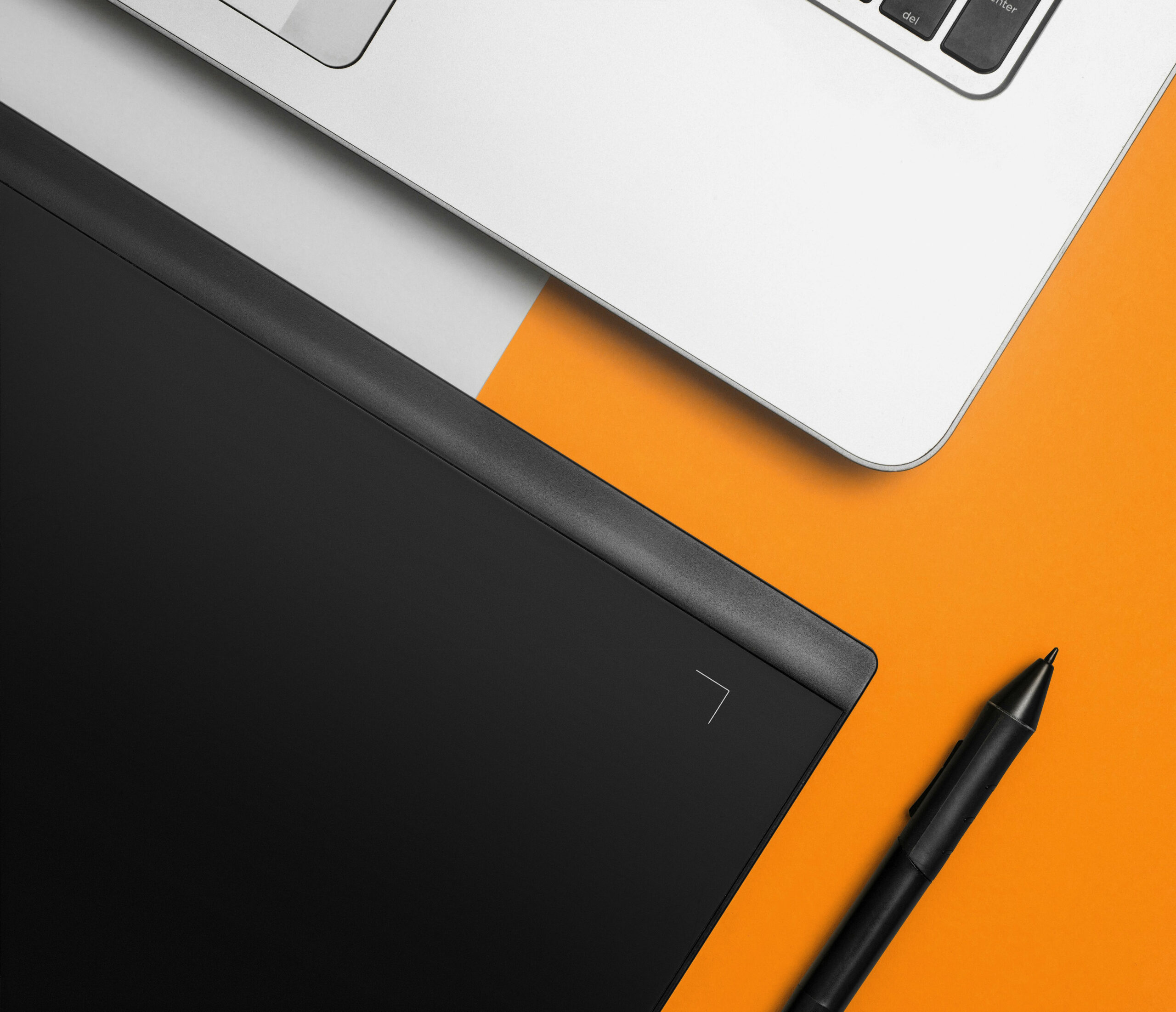 Flat lay of a laptop, digital drawing tablet, and stylus pen on an orange background, symbolising graphic design and creative digital work.