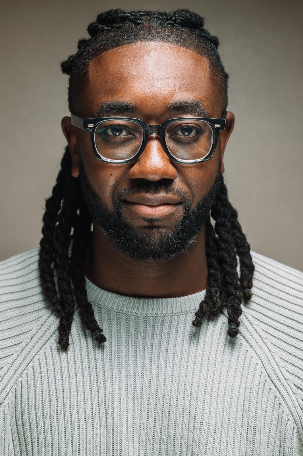Portrait of a man with dreadlocks wearing glasses.